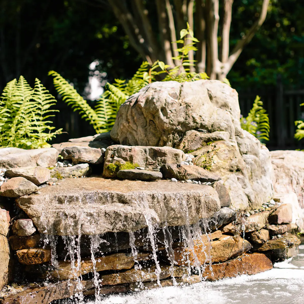 Stacked stone waterfall installed next to backyard pond