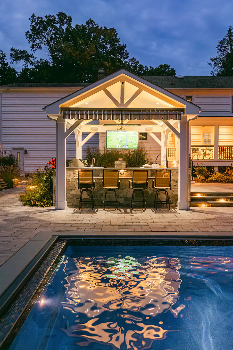 custom built pool with pavilion in backyard at night with warm lighting